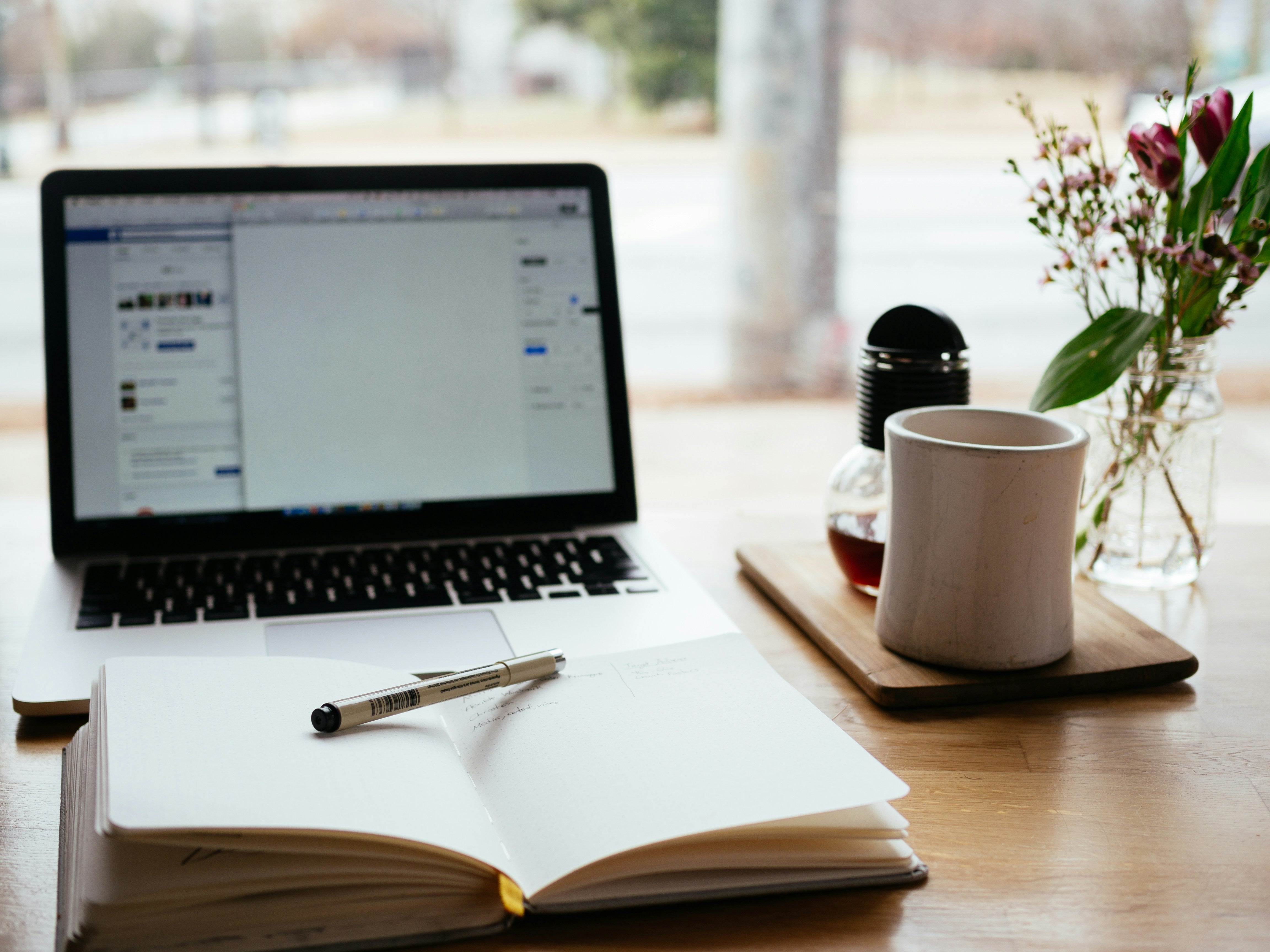 MacBook on a desk with a book and cup of coffee